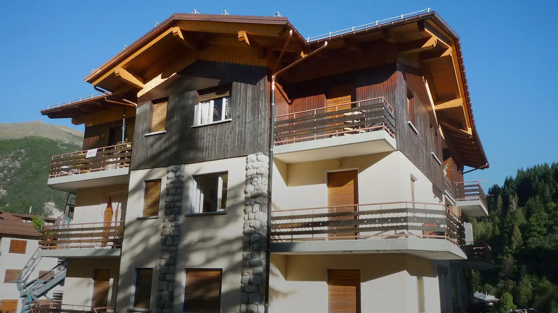 vista esterna del condominio con facciata in intonaco chiaro, ampi rivestimenti in legno scuro e balconi