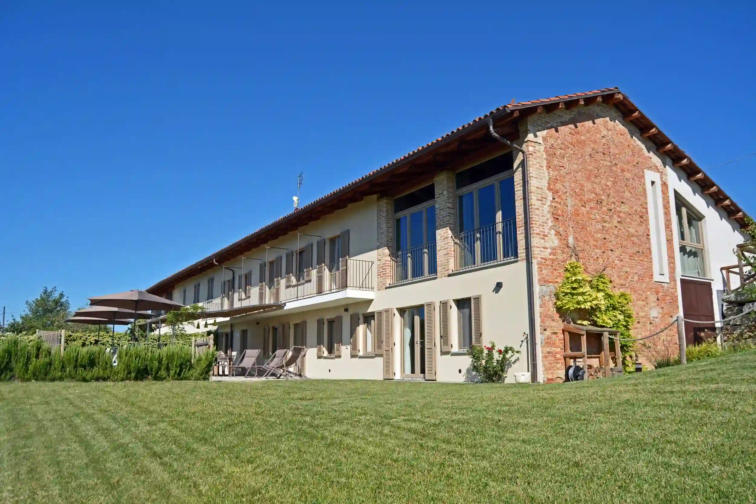 casale nelle langhe con facciata in mattoni e ampio giardino verde sotto cielo azzurro