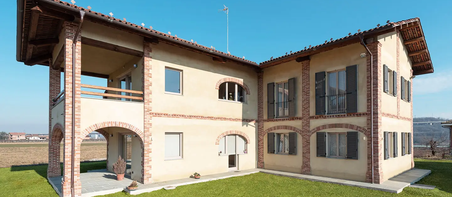 vista esterna dell'edificio ristrutturato con facciata panna, archi in mattoni a vista e persiane scure