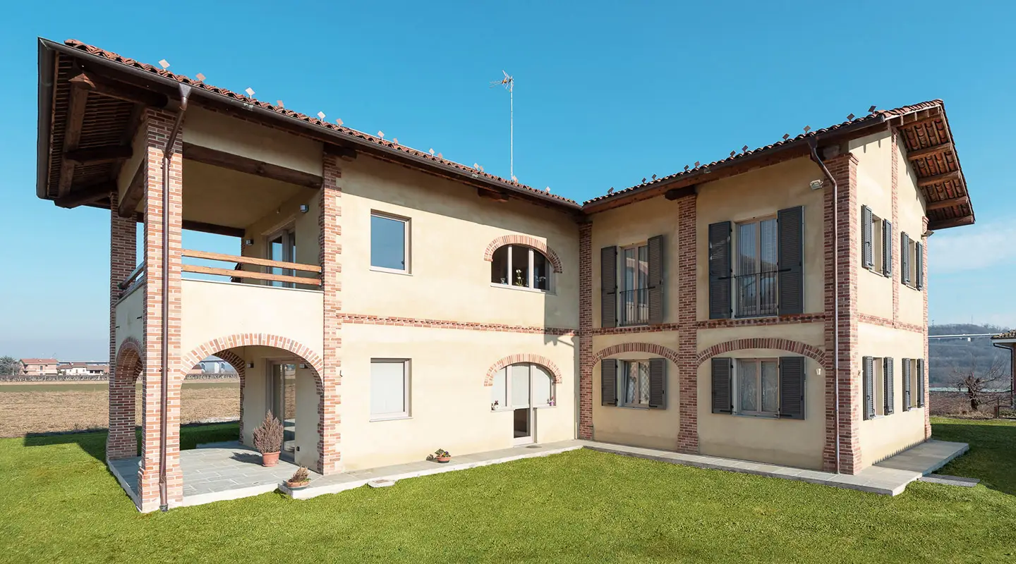 vista esterna dell'edificio ristrutturato con facciata panna, archi in mattoni a vista e persiane scure