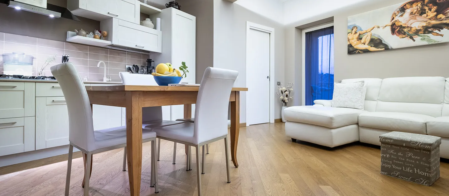 open space interno con zona pranzo, cucina moderna bianca e soggiorno con divano in pelle chiara