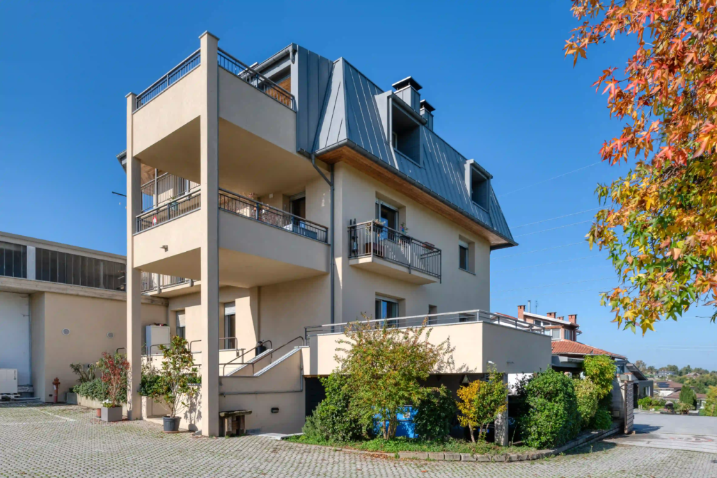 prospetto laterale di palazzina residenziale con tetto a mansarda in metallo grigio e facciata beige