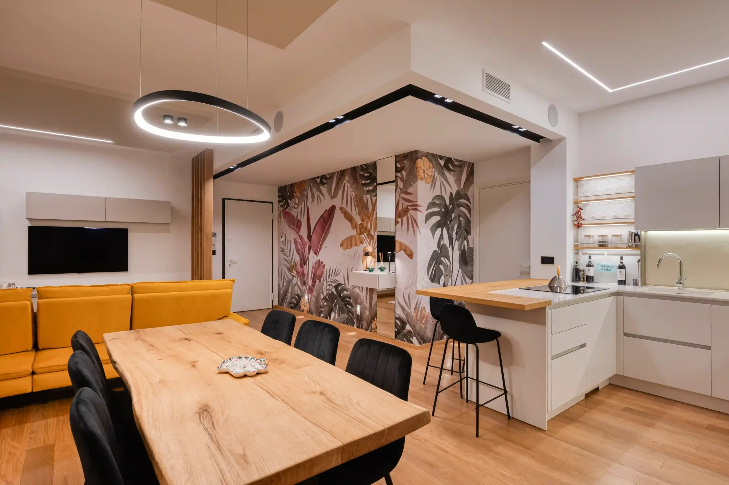 open space con zona living, tavolo in legno e cucina moderna con isola e carta da parati a motivi tropicali