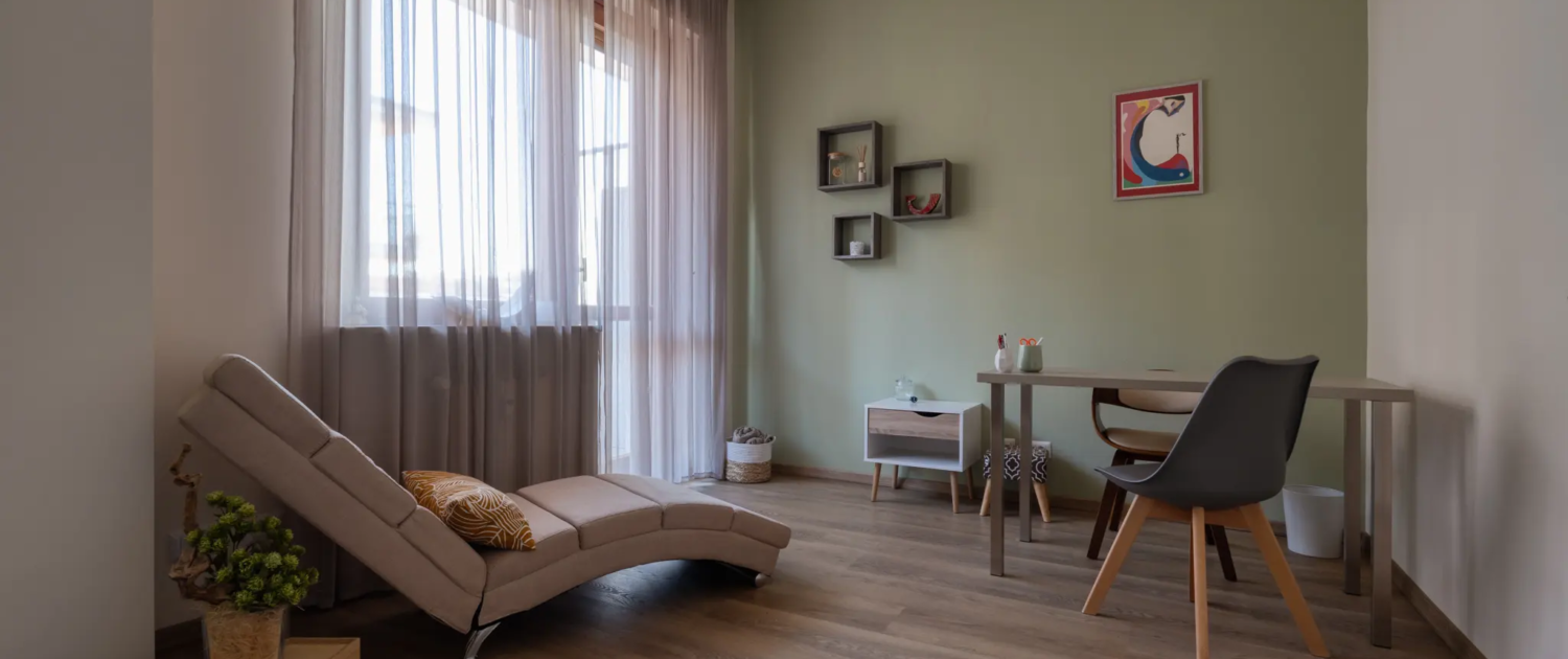 interno dello studio con scrivania minimalista con sedia grigia e ampie tende trasparenti che filtrano la luce