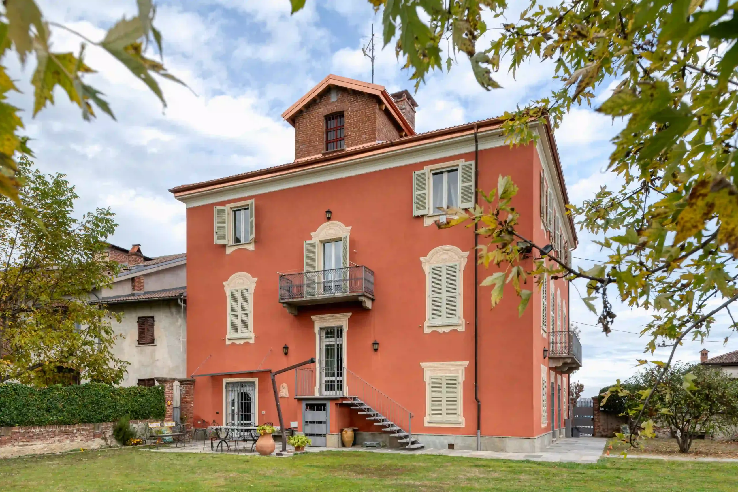 giardino interno con prato verde, zona relax e vista sulla facciata posteriore con scala metallica esterna e dettagli in rame sul tetto