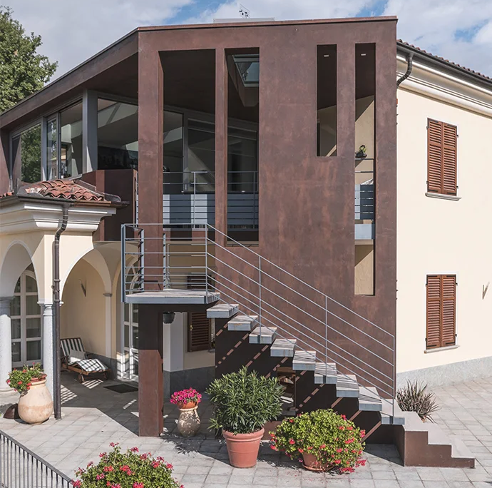 ampliamento moderno con finitura materica color corten, aperture verticali e scala in acciaio