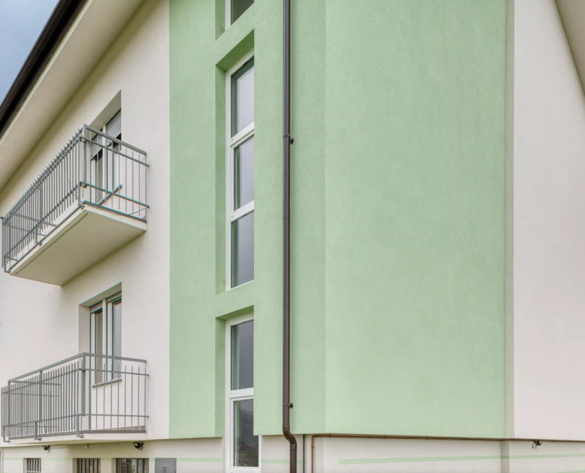 dettaglio architettonico della facciata con porzione verticale verde mela, ampie finestre e balconi in metallo grigio