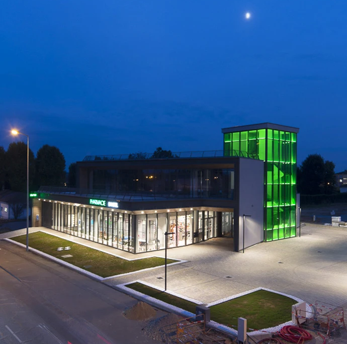 vista dell'edificio con focus sulla torre in vetro retroilluminata di verde e l'ampia area parcheggio illuminata