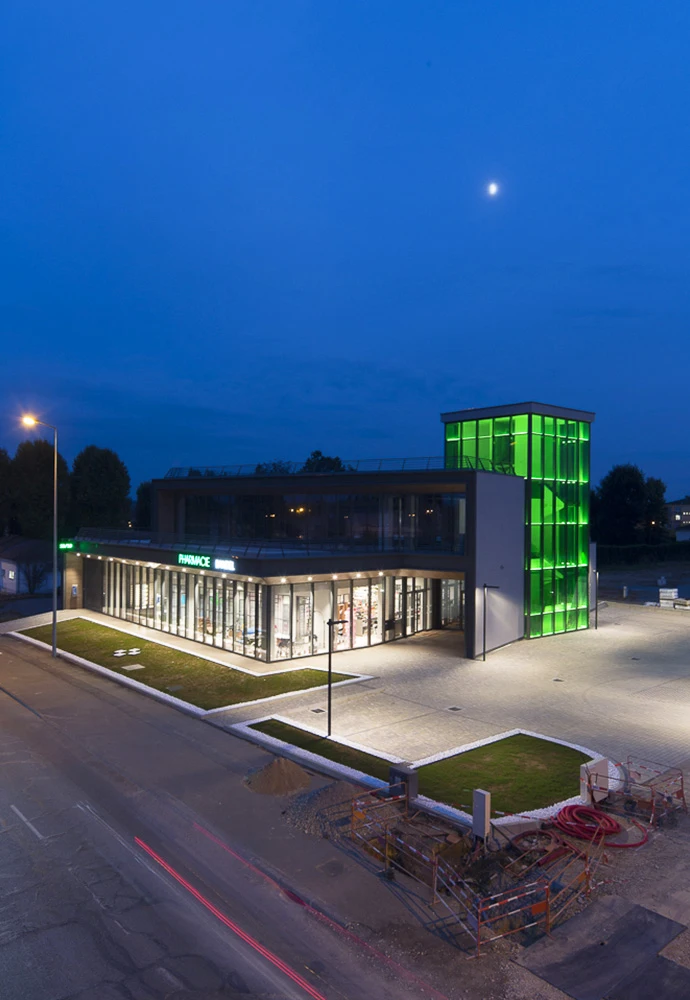 vista dell'edificio con focus sulla torre in vetro retroilluminata di verde e l'ampia area parcheggio illuminata