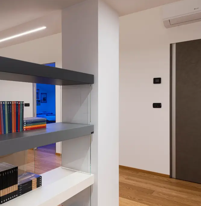 libreria moderna con montanti in vetro e ripiani grigi e bianchi, inserita accanto a un pilastro portante bianco