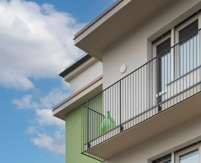 03_immagine_progetto_stella_alpina dettaglio ravvicinato dei balconi con parapetti minimali in metallo nero e una damigiana di vetro verde come decoro