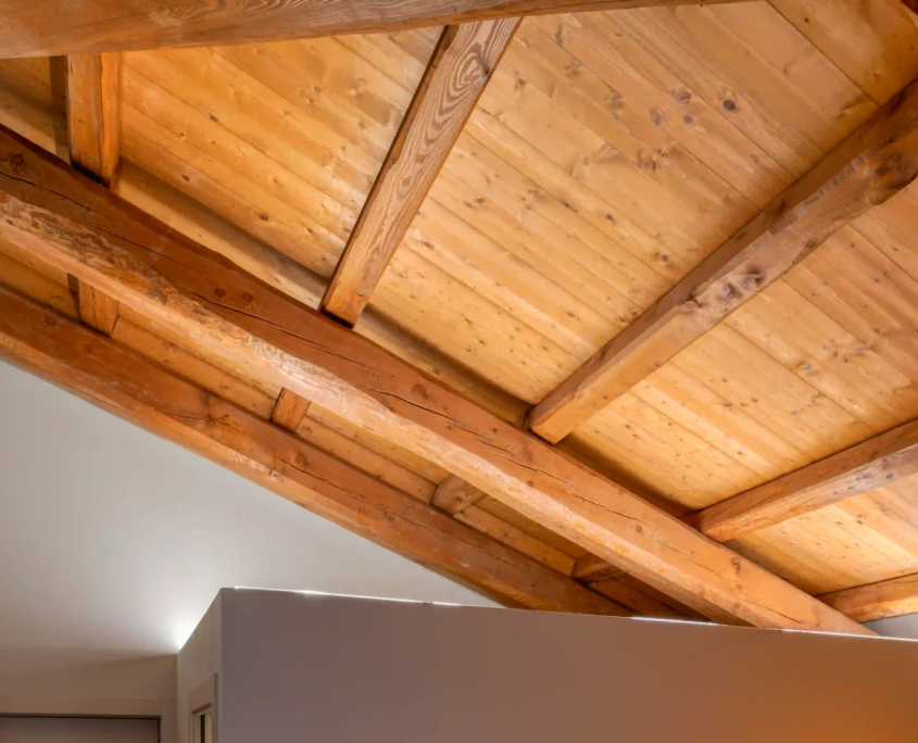 dettaglio del soffitto interno con travi in legno naturale a vista e sistema di illuminazione led lineare a incasso