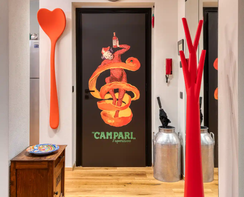 vista del disimpegno con porta artistica a tema campari, appendiabiti scultorei rossi e mobiletto antico in legno