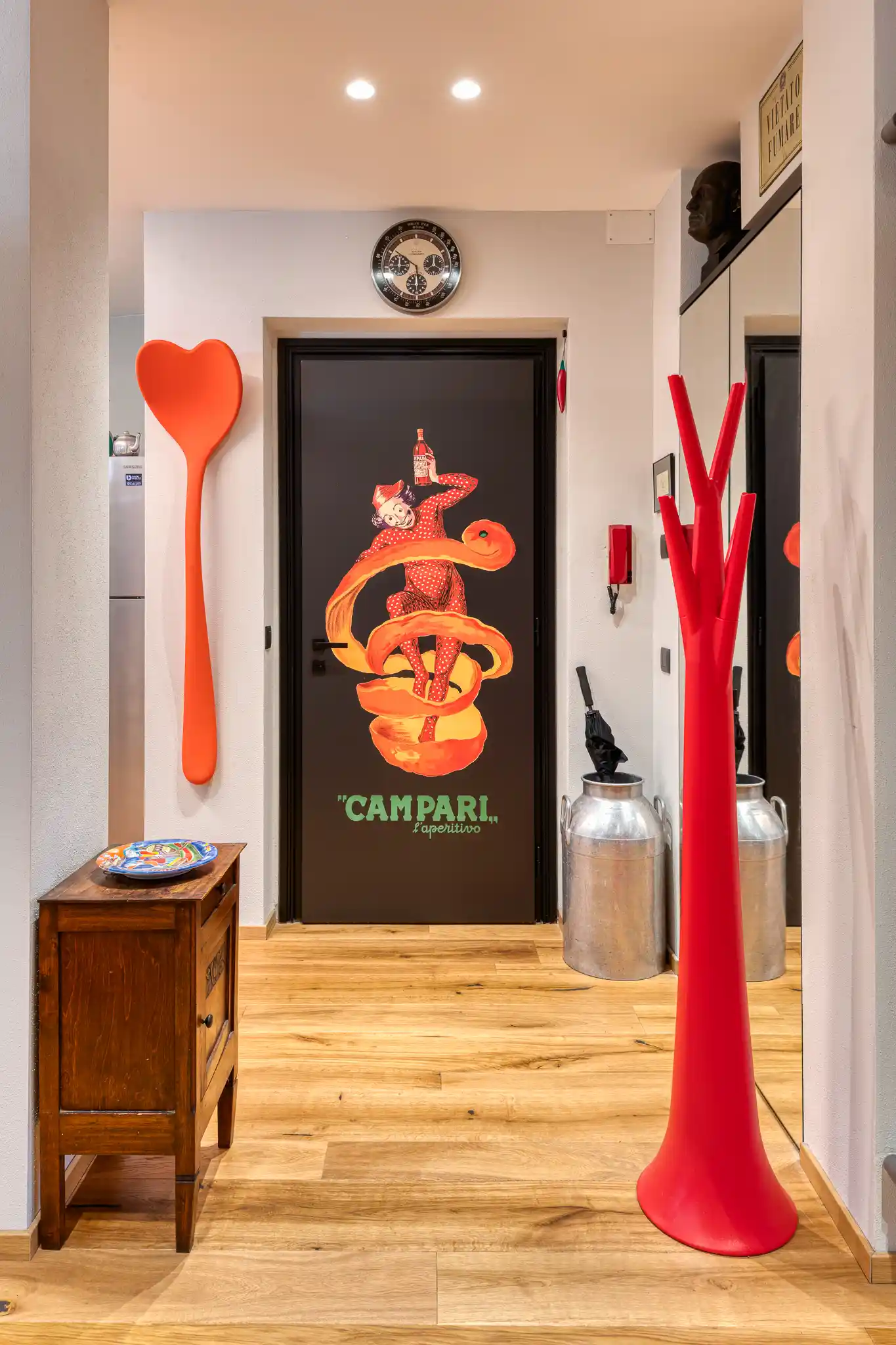 vista del disimpegno con porta artistica a tema campari, appendiabiti scultorei rossi e mobiletto antico in legno