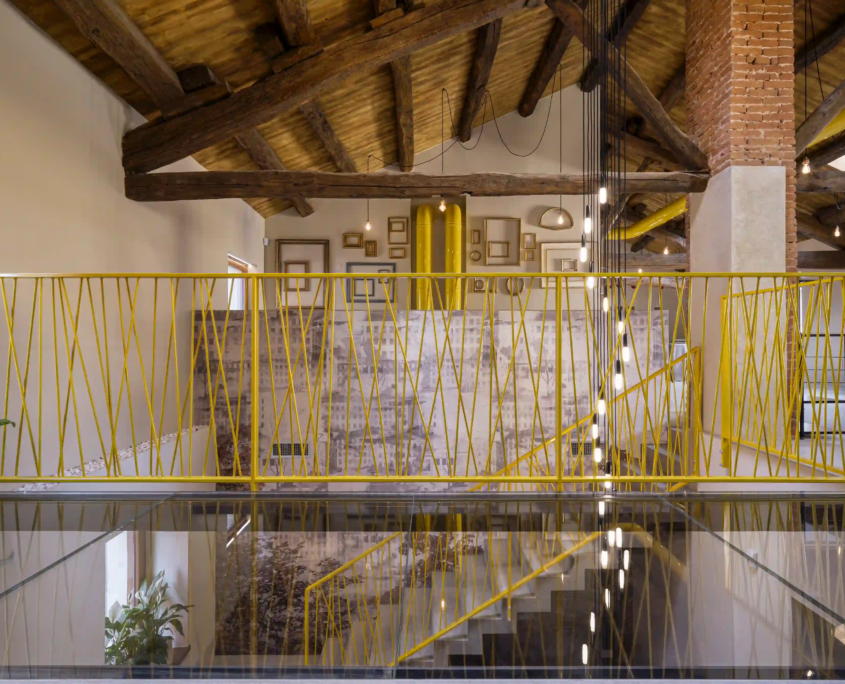 dettaglio architettonico del soppalco con pavimento in vetro, ringhiera metallica gialla e struttura del tetto in legno a vista