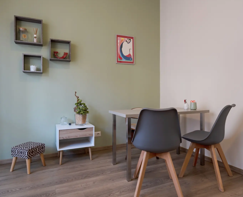 postazione di lavoro con scrivania moderna, sedie grigie e mensole a cubo scure sulla parete color verde salvia