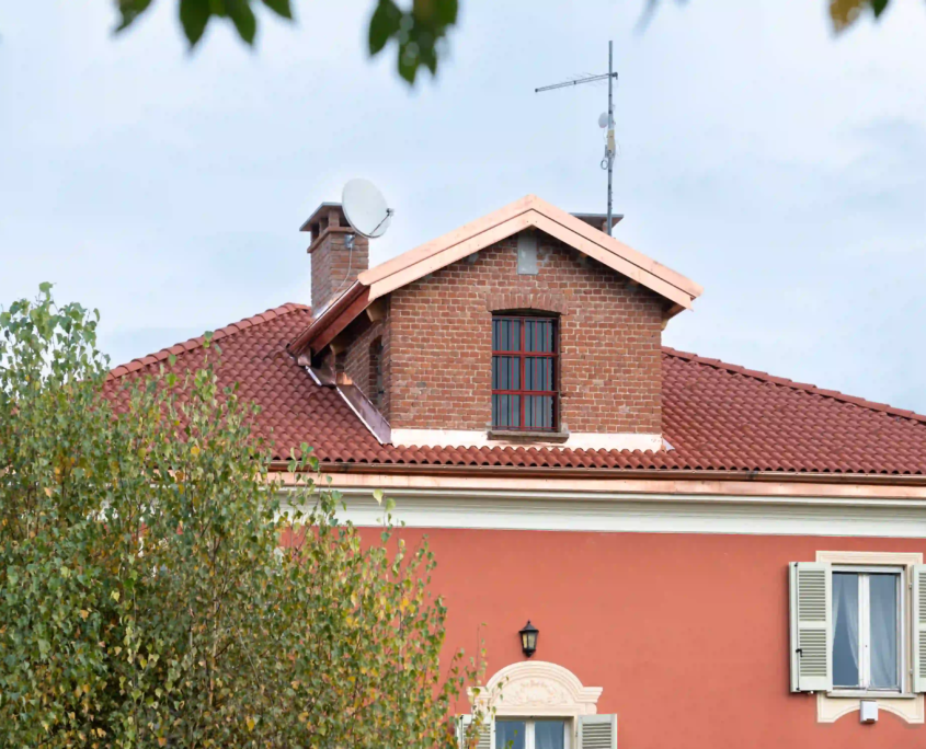 particolare della copertura con abbaino in mattoni, lattoneria in rame e installazione di parabola satellitare