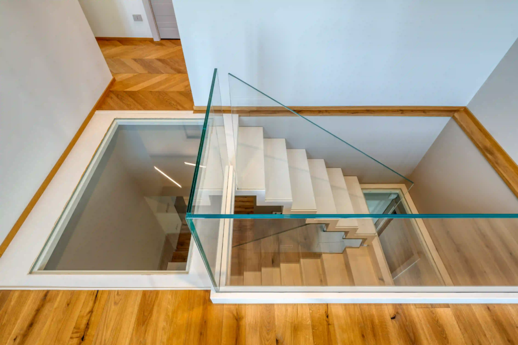 vista del vano scala moderno con gradini bianchi, parapetti in vetro trasparente e inserto in vetro calpestabile sul pianerottolo