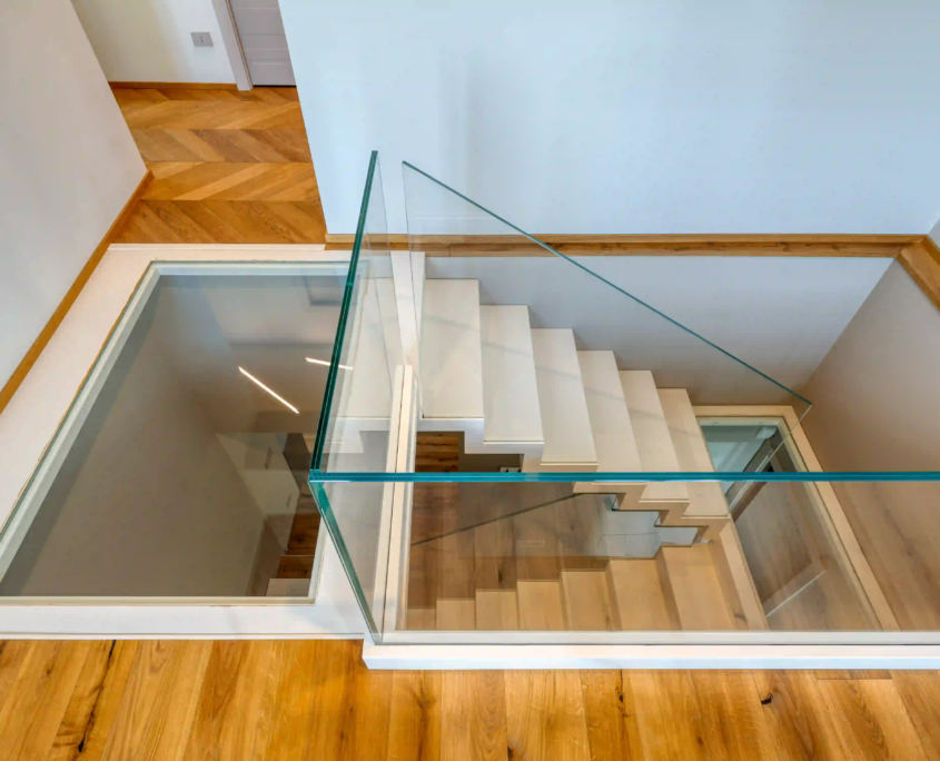 vista del vano scala moderno con gradini bianchi, parapetti in vetro trasparente e inserto in vetro calpestabile sul pianerottolo