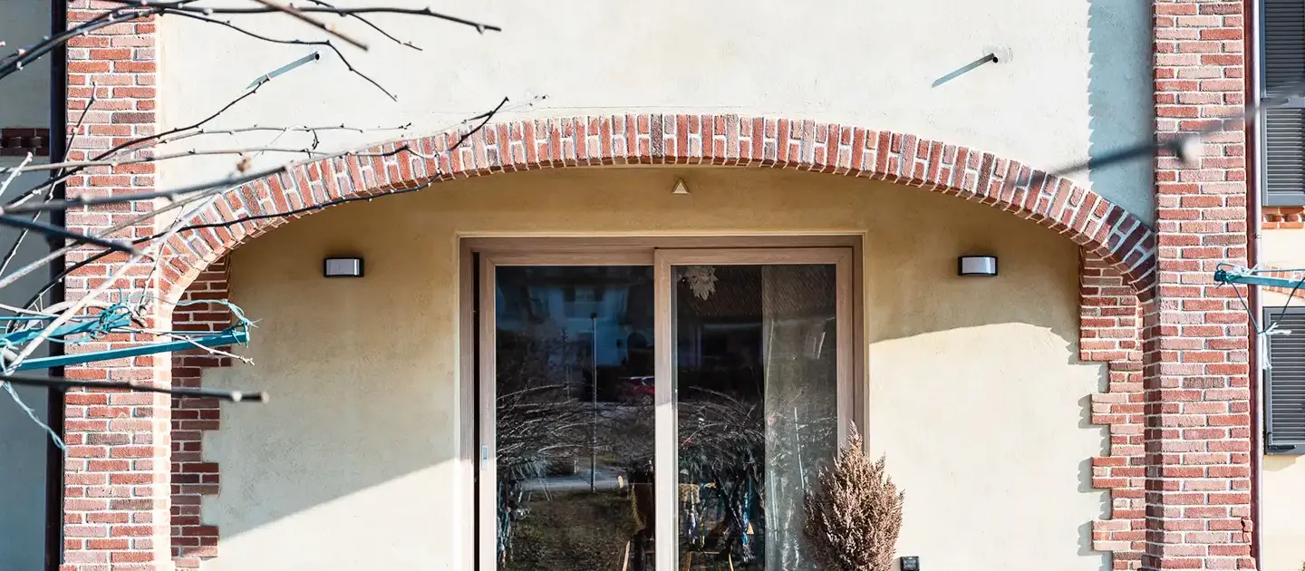 dettaglio dell'ingresso con serramento scorrevole moderno incorniciato da un grande arco strutturale in mattoni