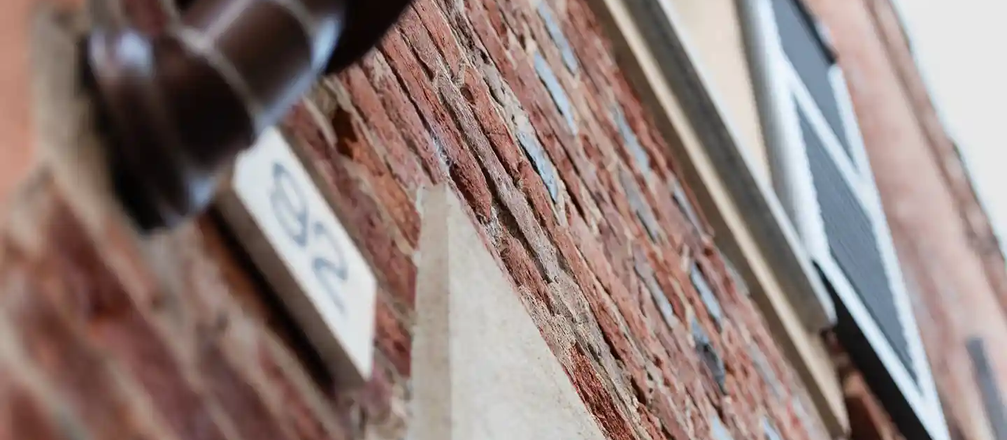 muro esterno in mattoni a vista con targa marmorea del numero civico e tubo pluviale scuro