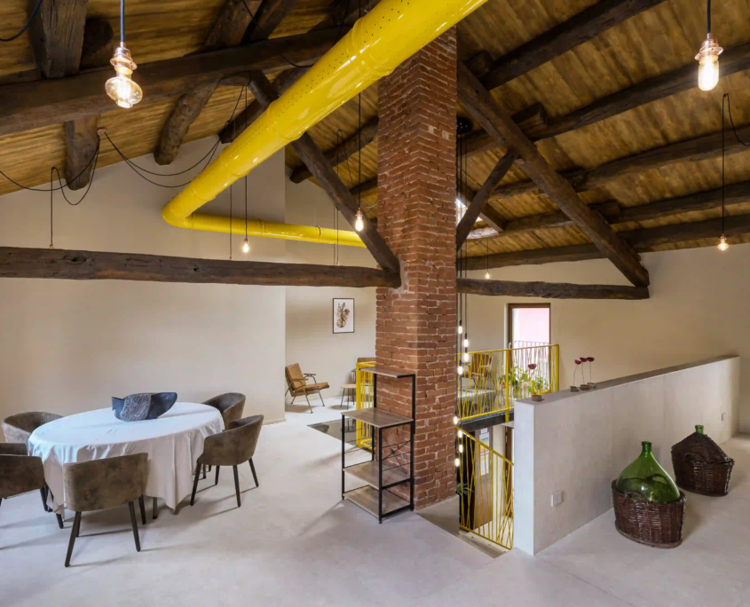vista della sala al piano superiore con pilastro portante in mattoni, tubazioni gialle a vista e lampade a sospensione minimali