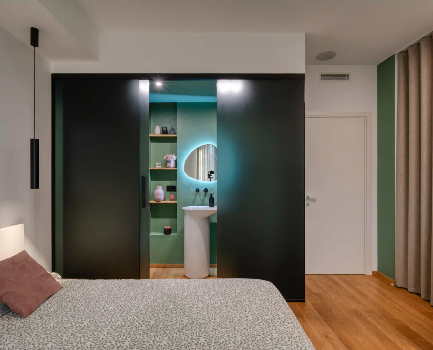 camera da letto con zona bagno integrata, ante scorrevoli scure e specchio retroilluminato