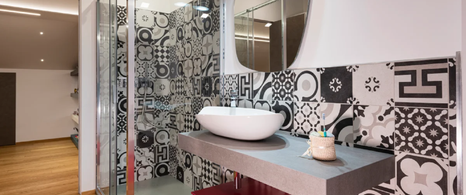 bagno con box doccia in vetro, rivestimento a parete con piastrelle a pattern geometrico e lavabo a bacinella