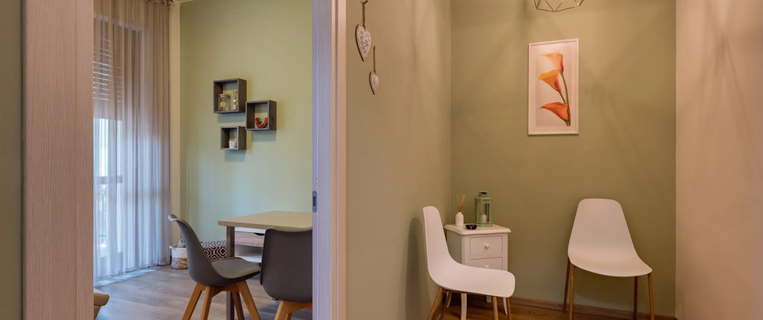 corridoio d'ingresso con pareti verdi, lampada a sospensione geometrica in metallo e sedute per l'attesa bianche
