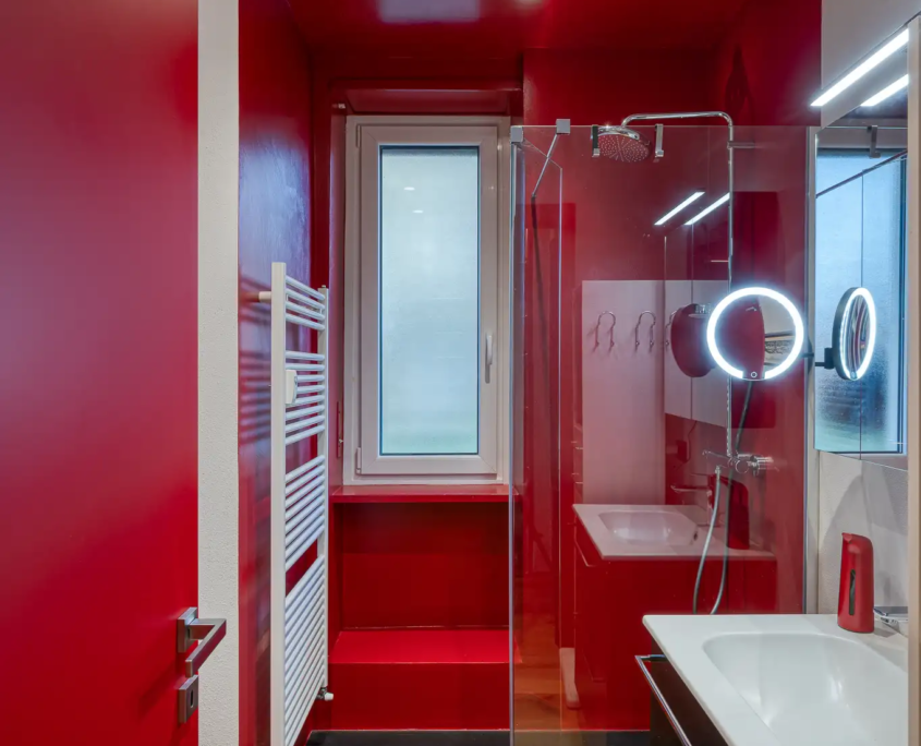 bagno moderno con pareti e soffitto rosso lucido a contrasto, box doccia in cristallo e arredi minimalisti