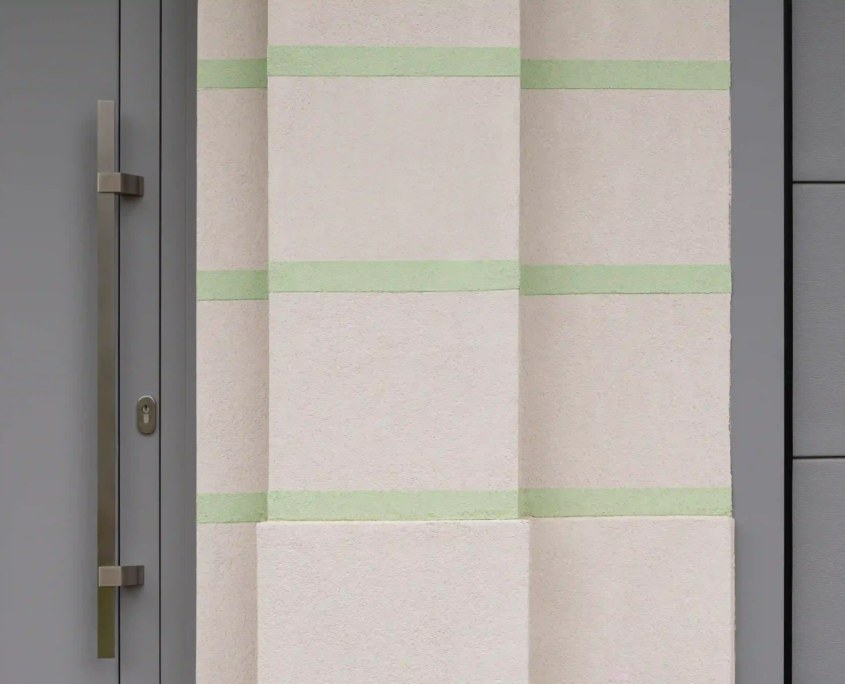 dettaglio dell'ingresso con porta moderna grigia, maniglione verticale in acciaio e decorazione murale a fasce orizzontali verdi