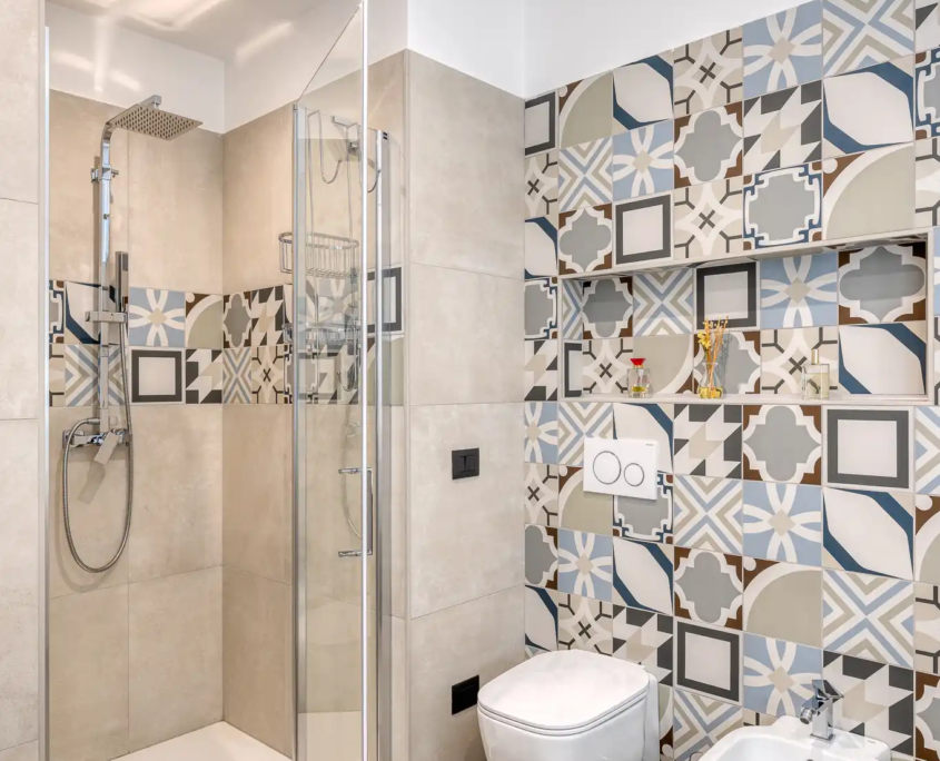 interno bagno con box doccia, rivestimento in piastrelle decorate a pattern geometrico e sanitari bianchi