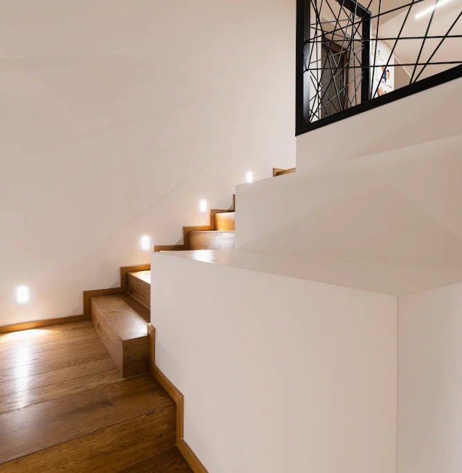scala interna con gradini in legno naturale e struttura in muratura bianca, illuminata da faretti a incasso laterali