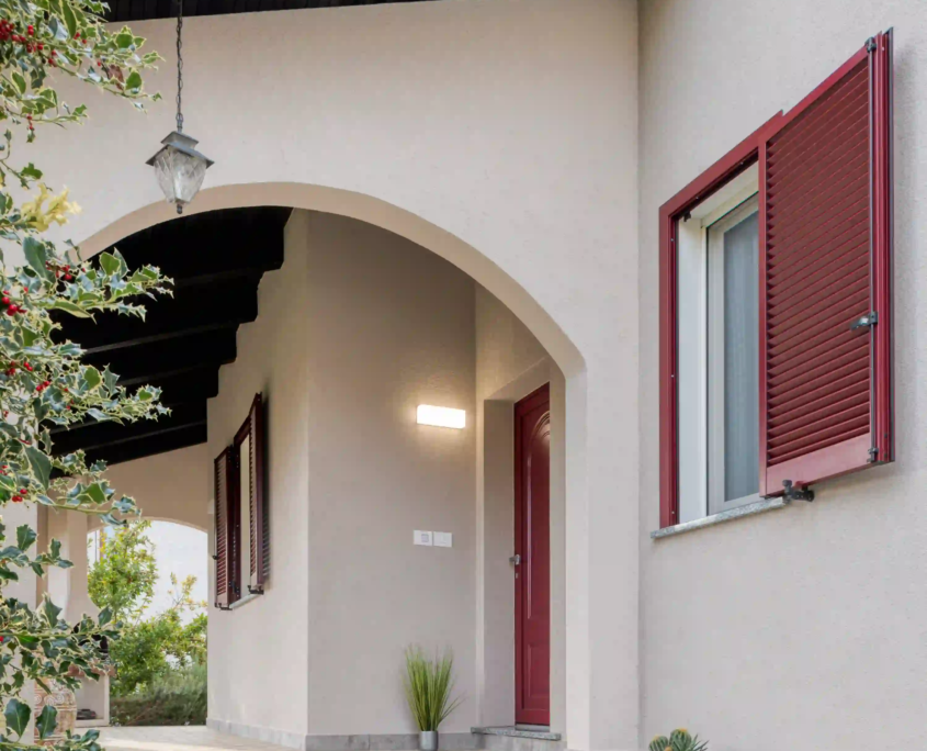 portico esterno con archi, persiane rosse e ingresso su casa in stile tradizionale