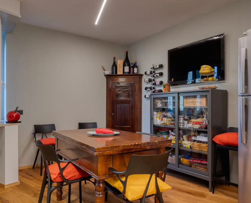 zona pranzo con tavolo in legno, sedie moderne nere con cuscini colorati e vetrinetta industriale grigia