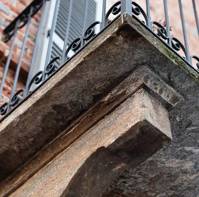 vista dal basso di una mensola in pietra a sostegno di un balcone storico con ringhiera in ferro