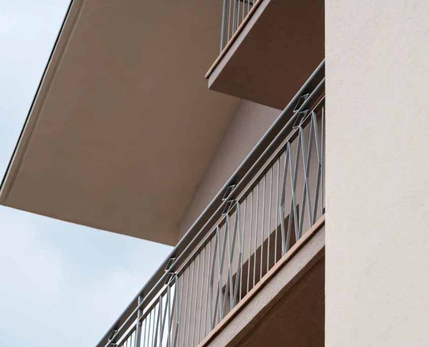primo piano della ringhiera del balcone in metallo grigio con motivo decorativo a rombi e dettaglio del bordo del solaio