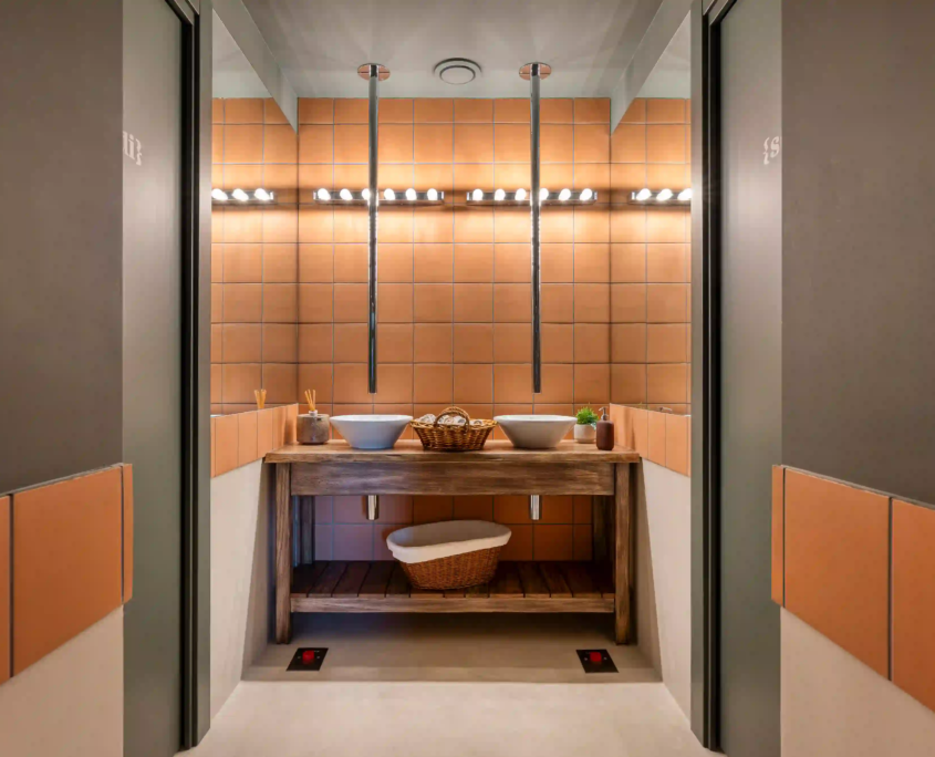 zona lavabo del bagno con due lavandini bianchi su piano in legno, rubinetteria a soffitto e piastrelle quadrate color terracotta
