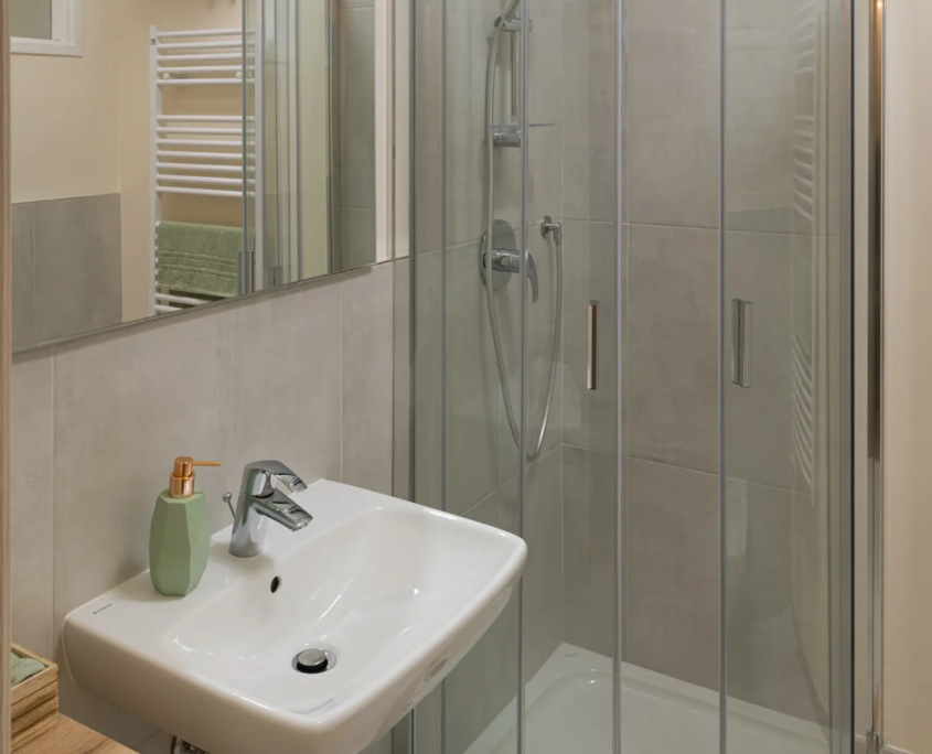 dettaglio del bagno con box doccia angolare in vetro e rivestimenti color grigio e verde menta