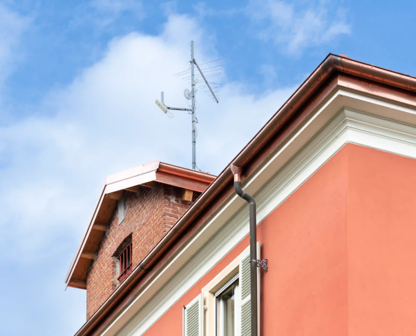 dettaglio architettonico del tetto con pluviale in rame, antenna tv e finitura della facciata color arancio
