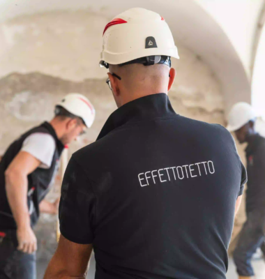 operaio che livella il cemento in un locale con pareti in mattoni a vista, soffitto a volta e stivali gialli durante lavori di ristrutturazione