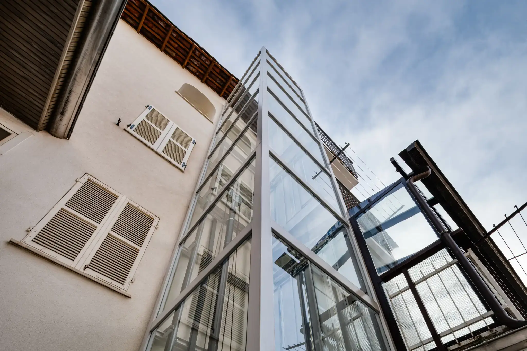 ascensore esterno in vetro e metallo bianco realizzato su edificio d epoca visto dal basso per abbattimento barriere architettoniche
