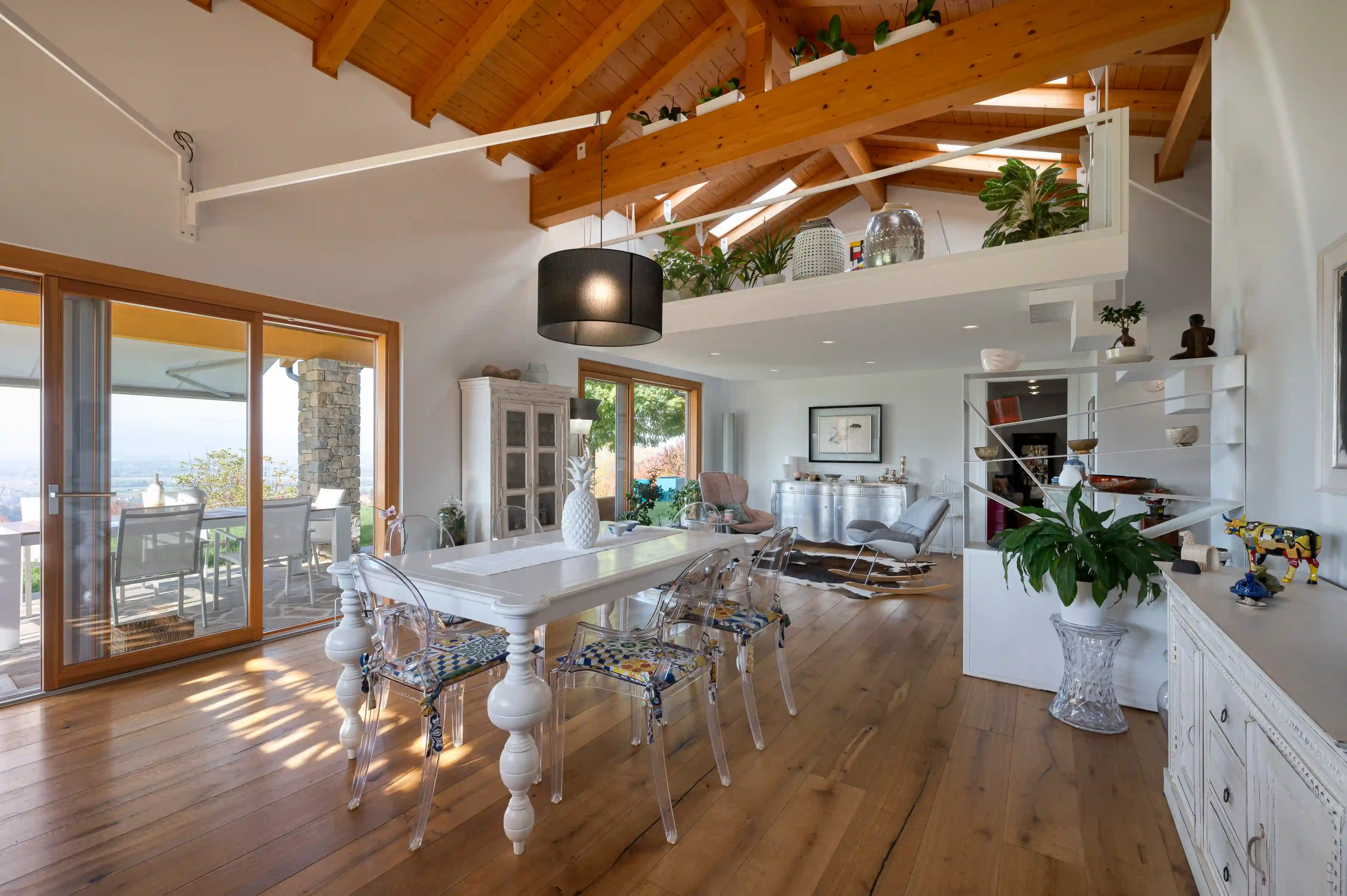 open space interno con soffitto in legno, tavolo da pranzo bianco e soppalco a vista